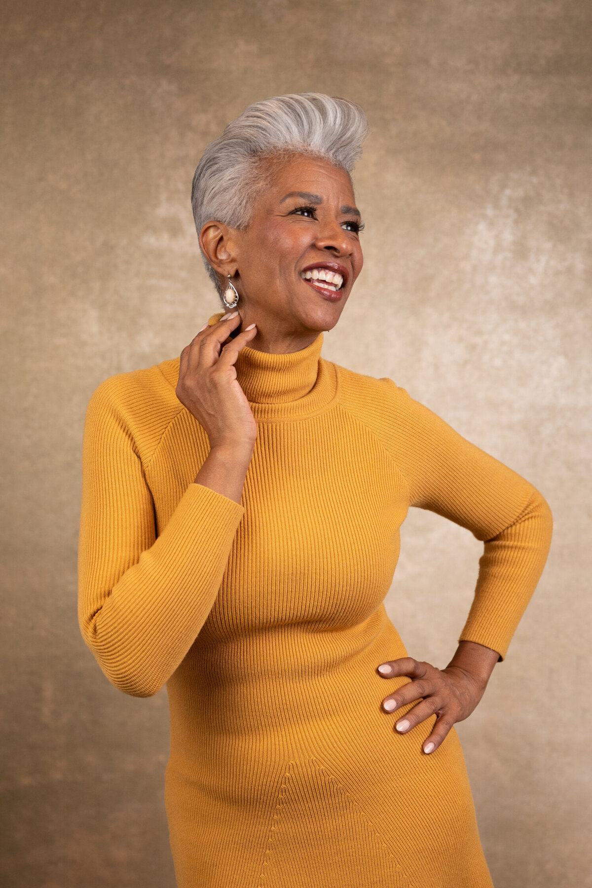 a woman with short grey hair posing smiling wearing a yellow thigh dress