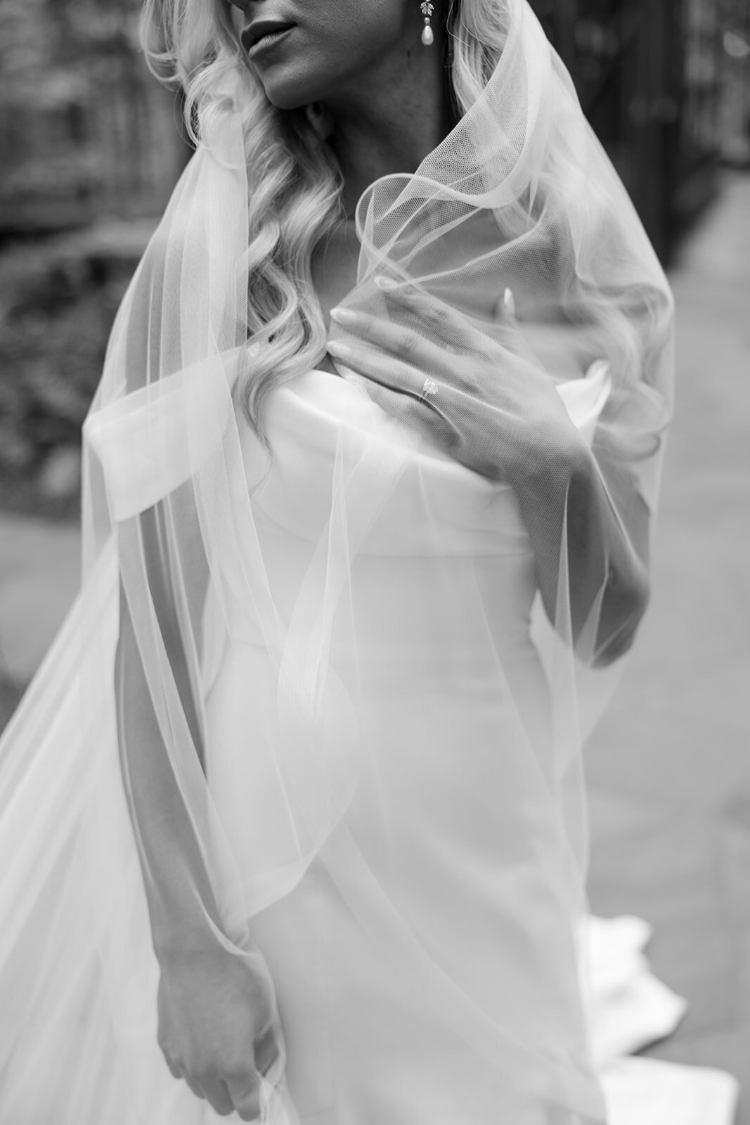 Bride wrapped in her veil showing off her wedding ring looking to the side.