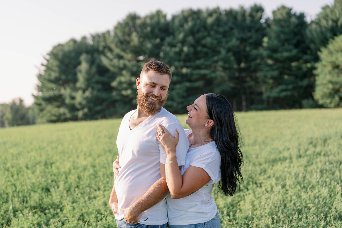 Kali and Joe laughing together in a tall grassy field on a private property near Detroit during their engagement session.