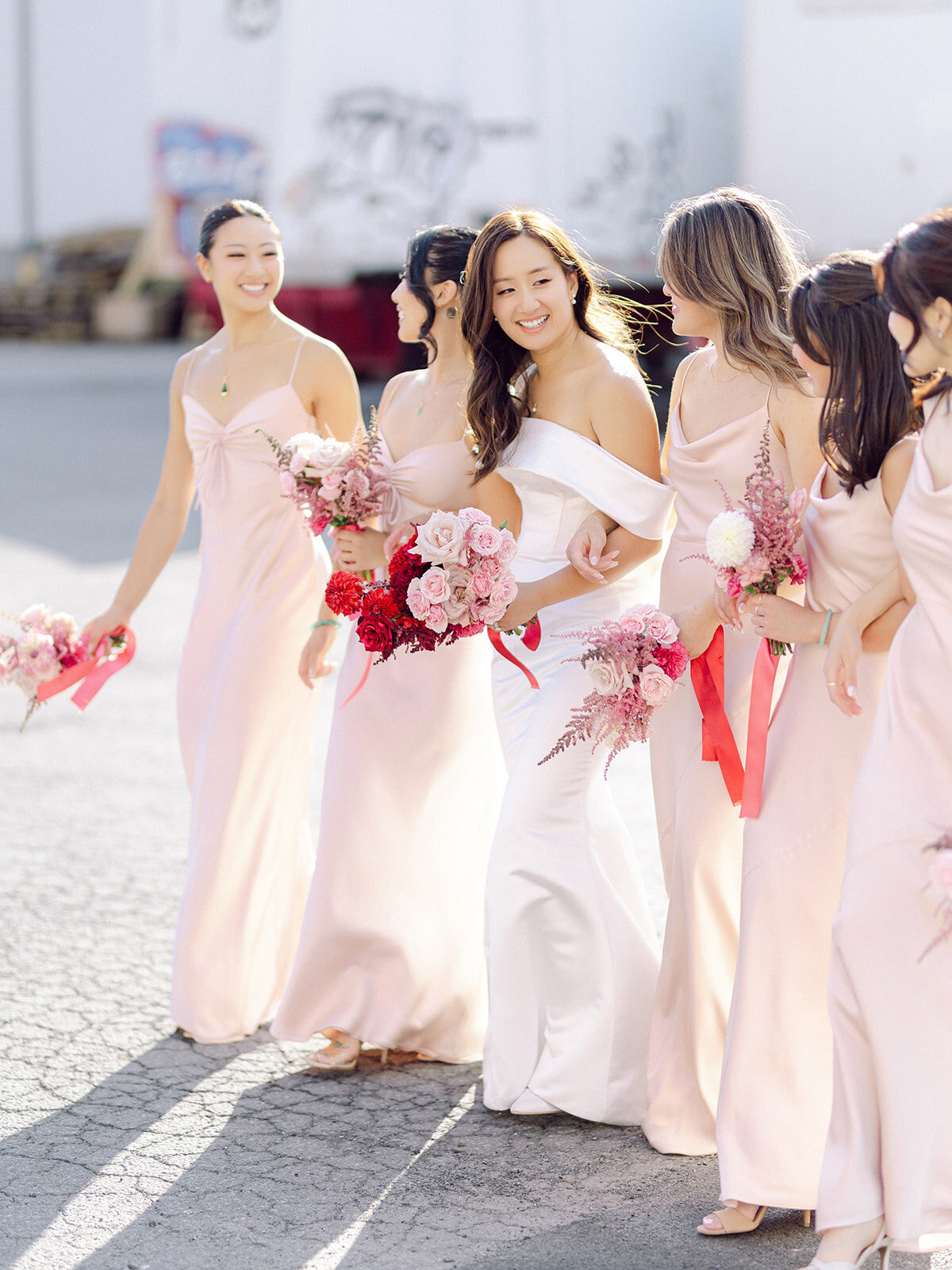 A bridal party hold bouquets of pink flowers in front of The Rye.