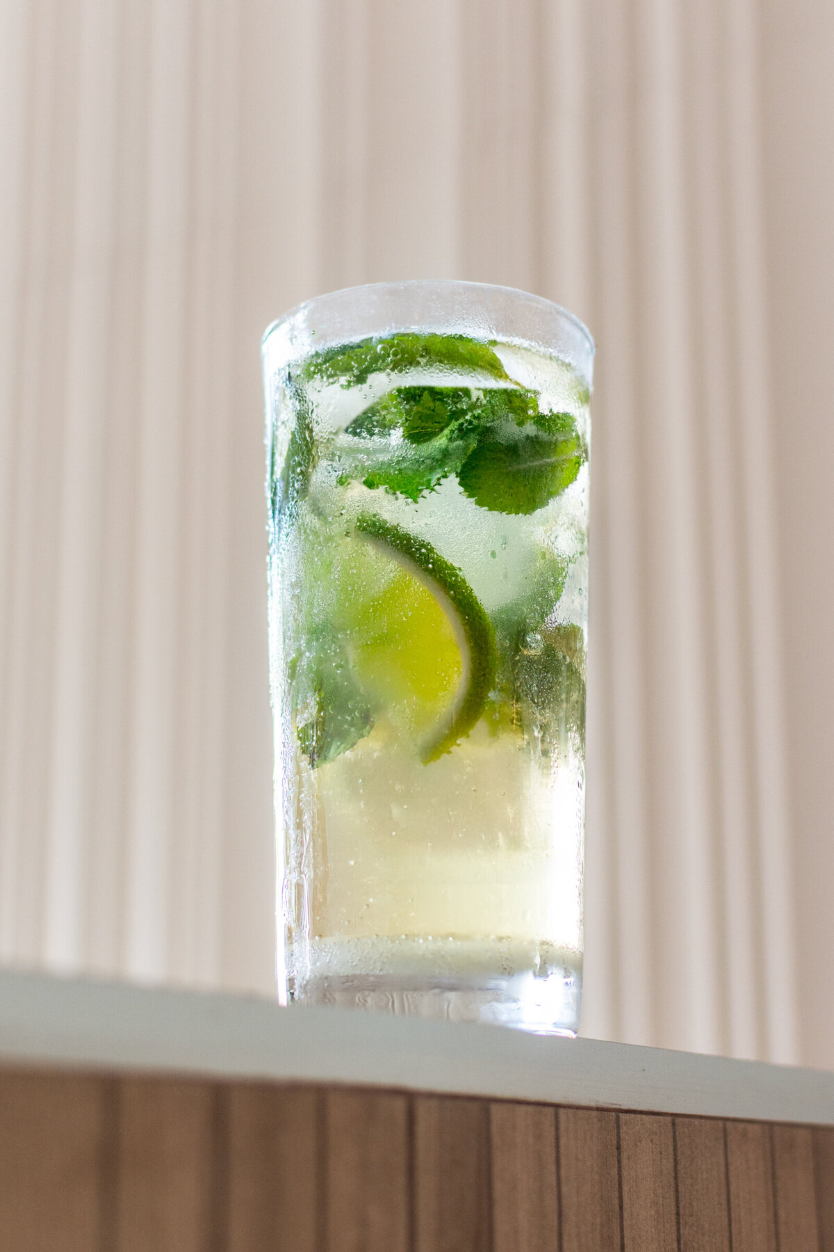 A white rum mojito with mint leaves, lime wedges, and photographed against a white textured wall.