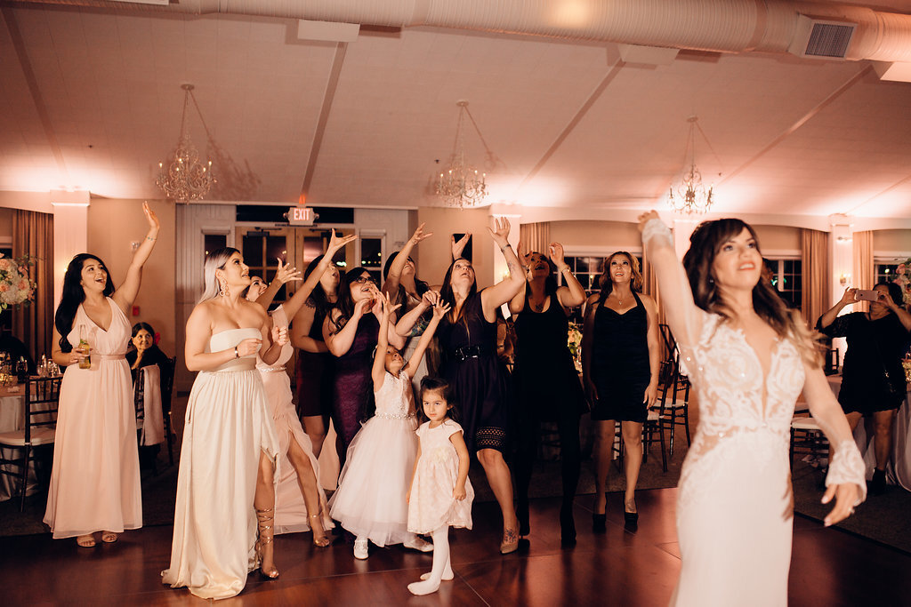 Wedding Photograph Of Women In White And Maroon Dresses Raising Their Hands To Catch The Bouquet Los Angeles