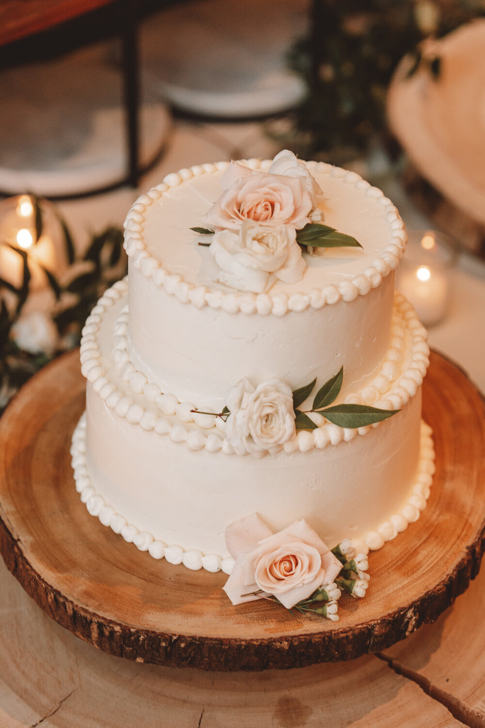 Elegant white wedding cake with blush florals on a rustic wood stand at a fall wedding in Kimpton Armory, Bozeman, MT.