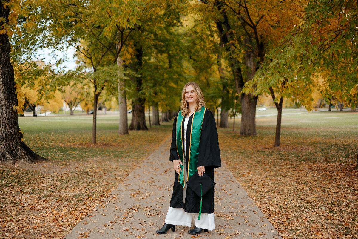 A Colorado State University graduate poses for a portrait on The Oval in Fort Collins, Colorado, during the fall.