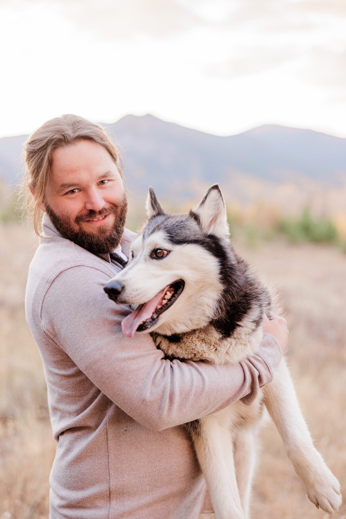 A smiling father hugs his husky in a grey shirt