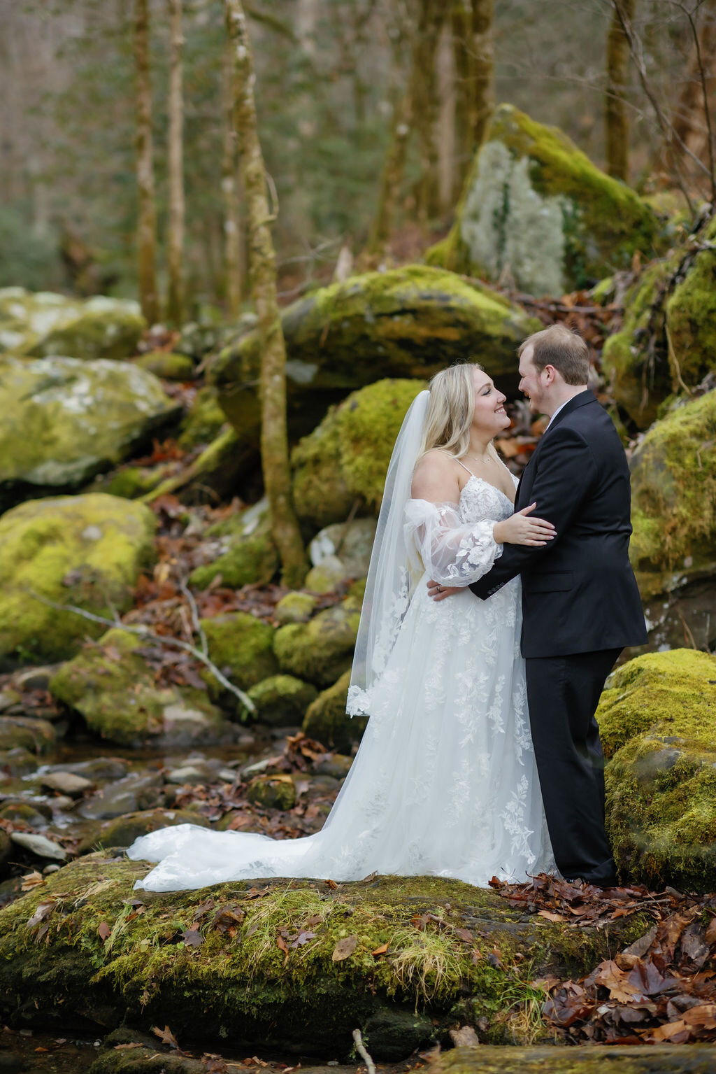 gatlinburg photographers captures forest elopement in the Smoky Mountains with couple holding each other in front of mossy rocks in the woods 