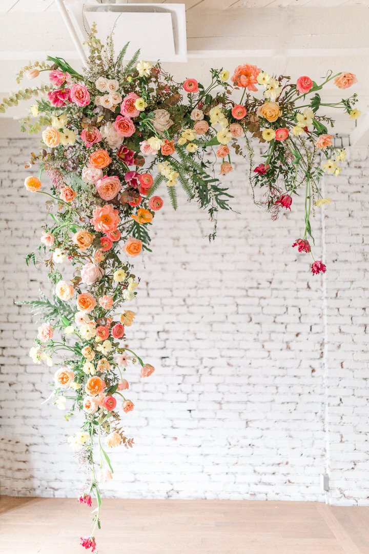 Bright cascading ceremony arrangement suspended in front of a white brick wall at a Montreal wedding. 