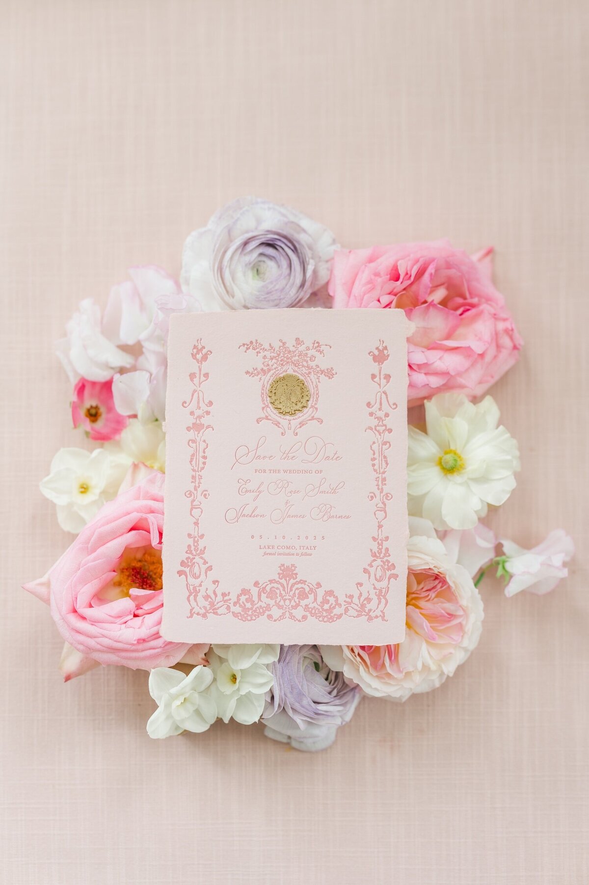 A pink save the date flat lay surrounded by florals 