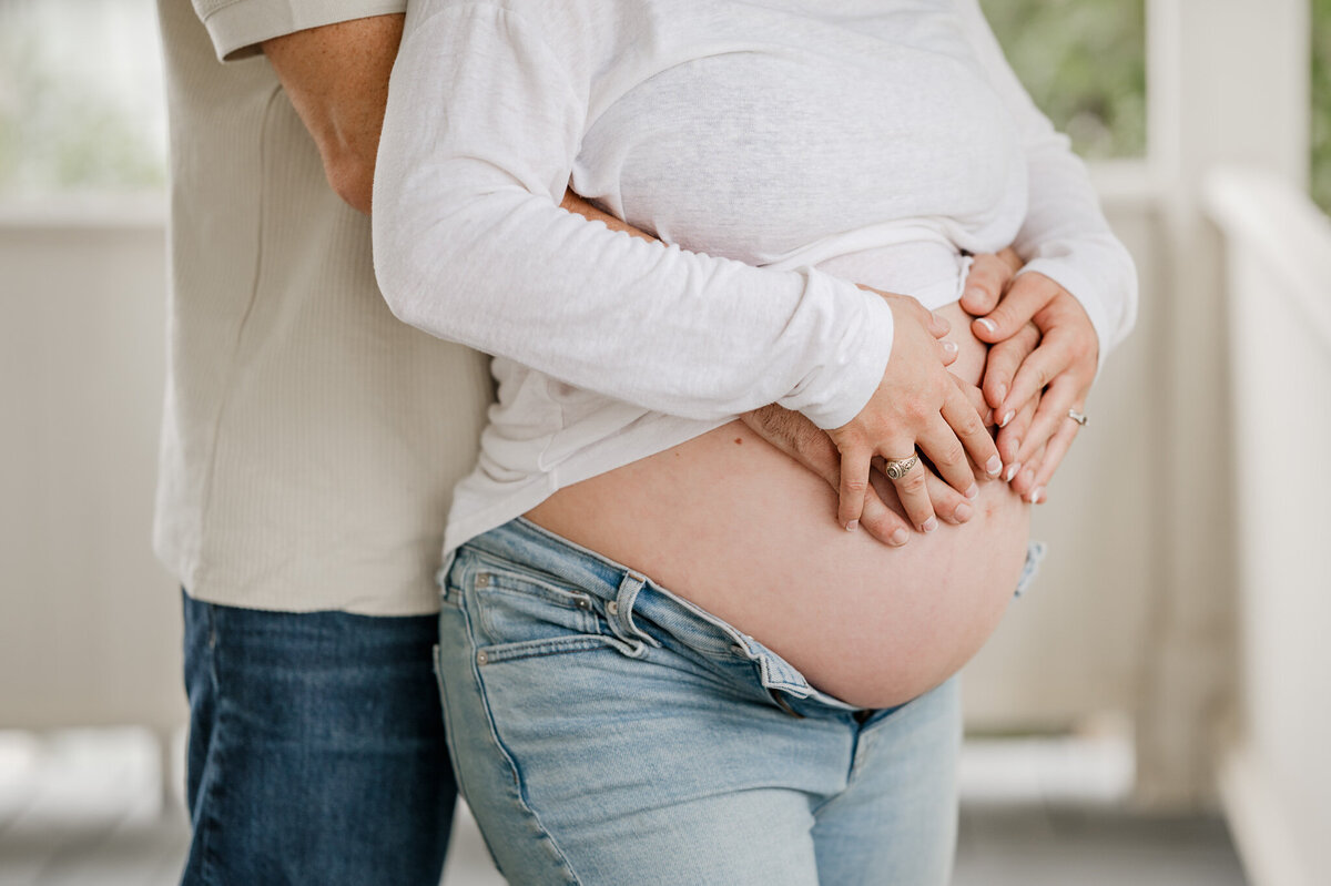 Close-up of a man and woman holding hands on her pregnant tummy.