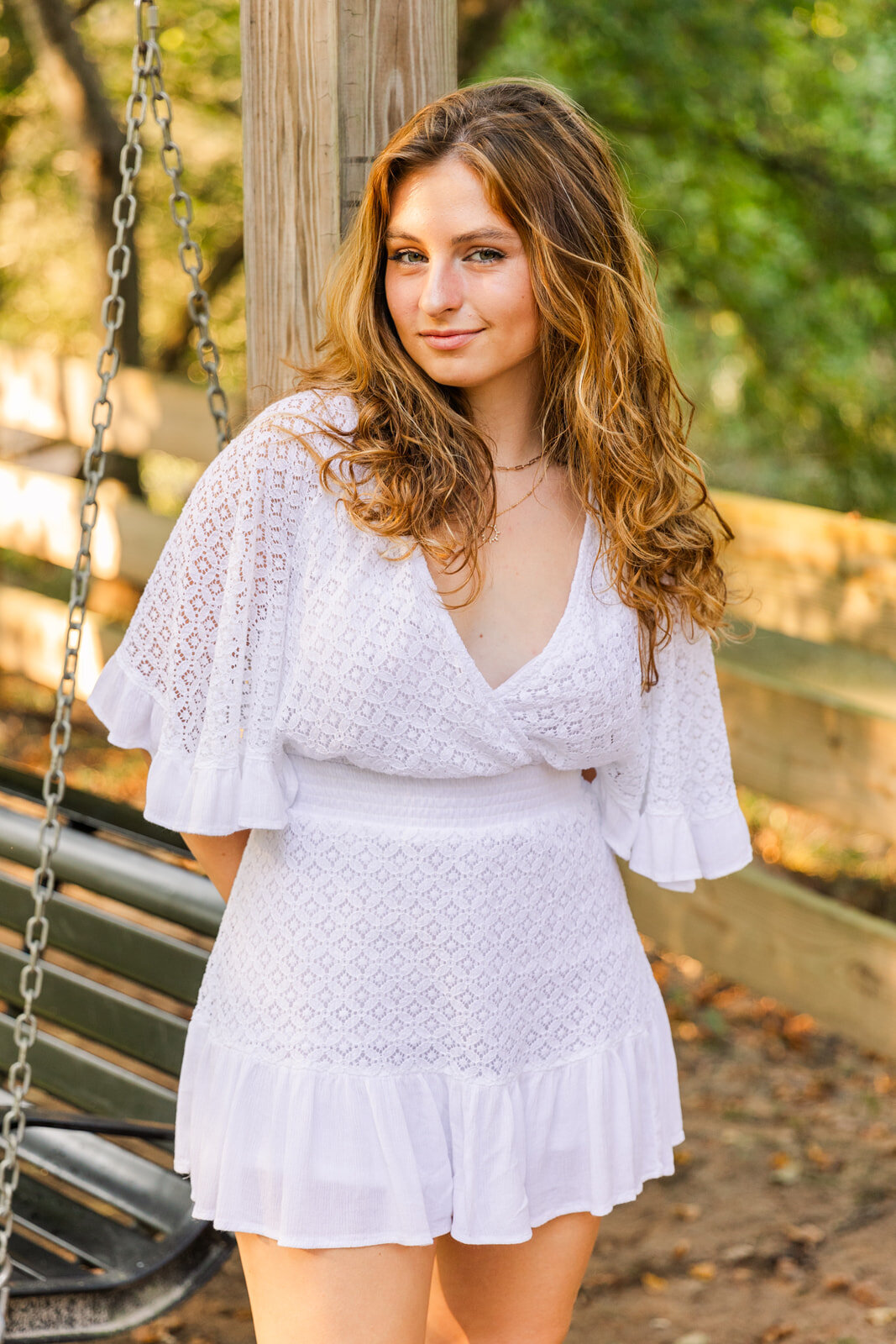 senior girl leaning on a wooden pole hands back looking at the camera during photo session