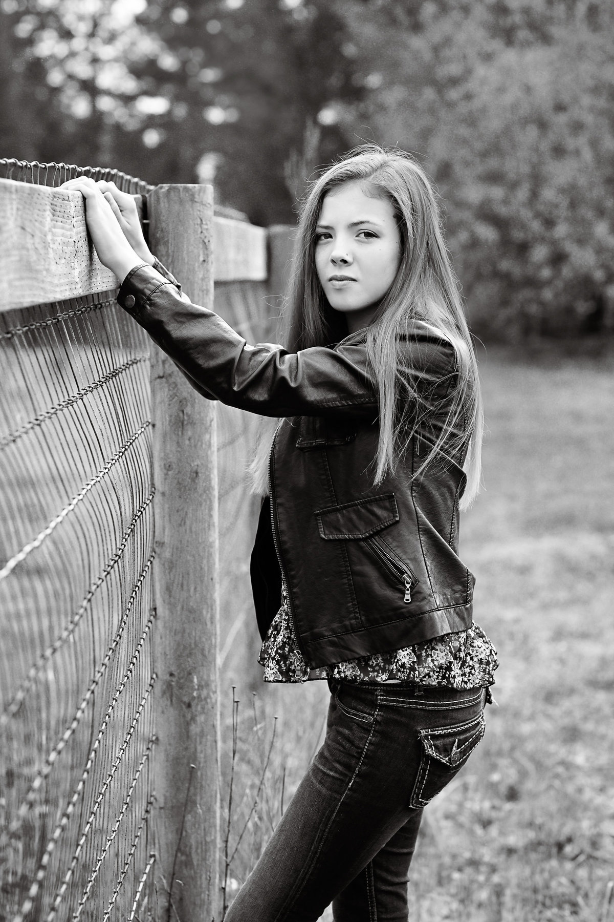 Fashion styled image of a senior girl in a leather jacket with a fence