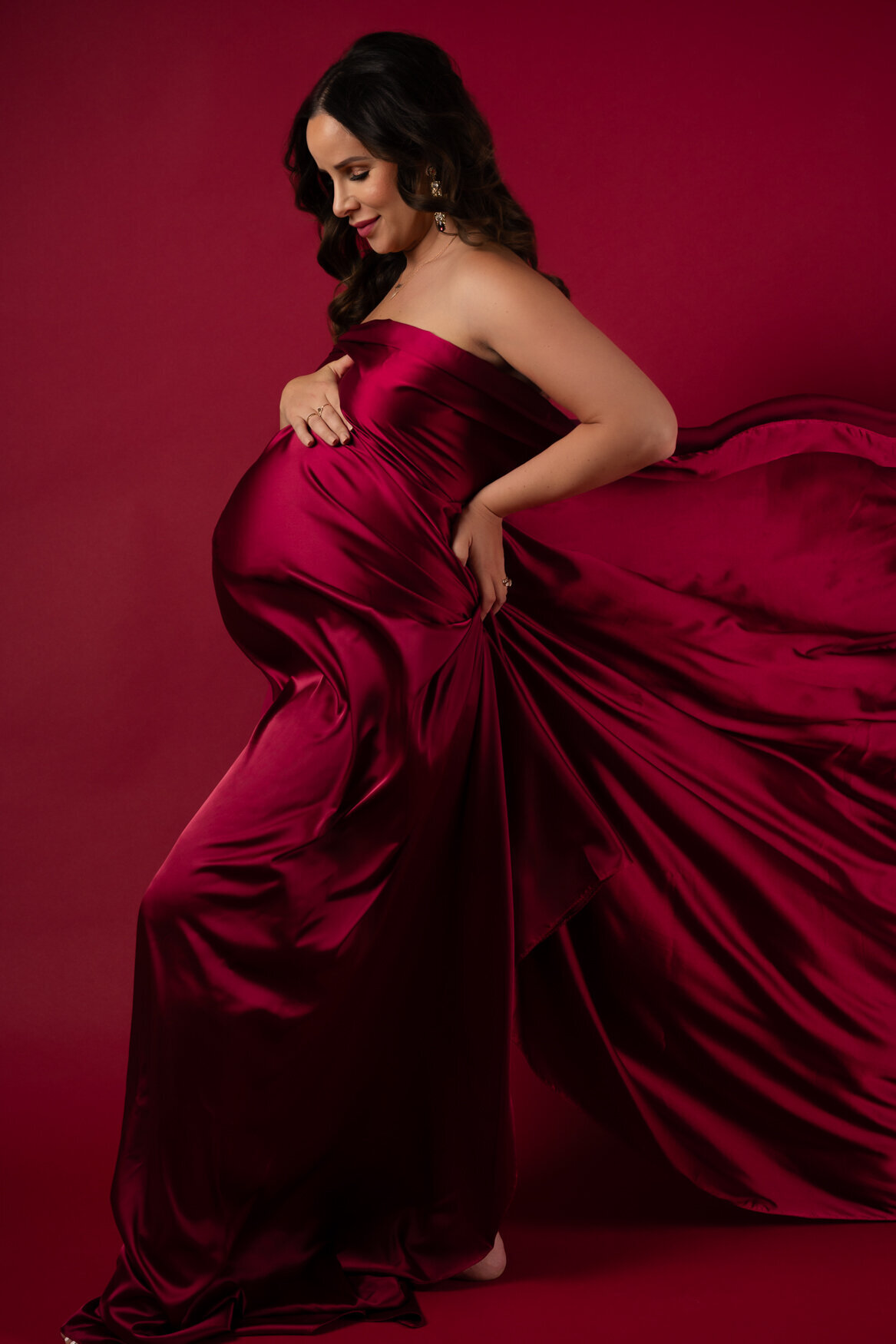 portrait of a pregnant woman cover in a red satin fabric looking down at her belly