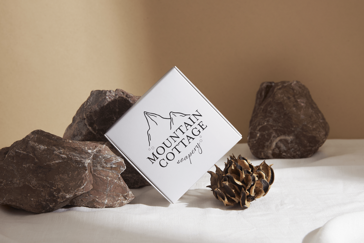 A logo for a soap company called moutain cottage soapery is mocked up on a box with rustic rock background