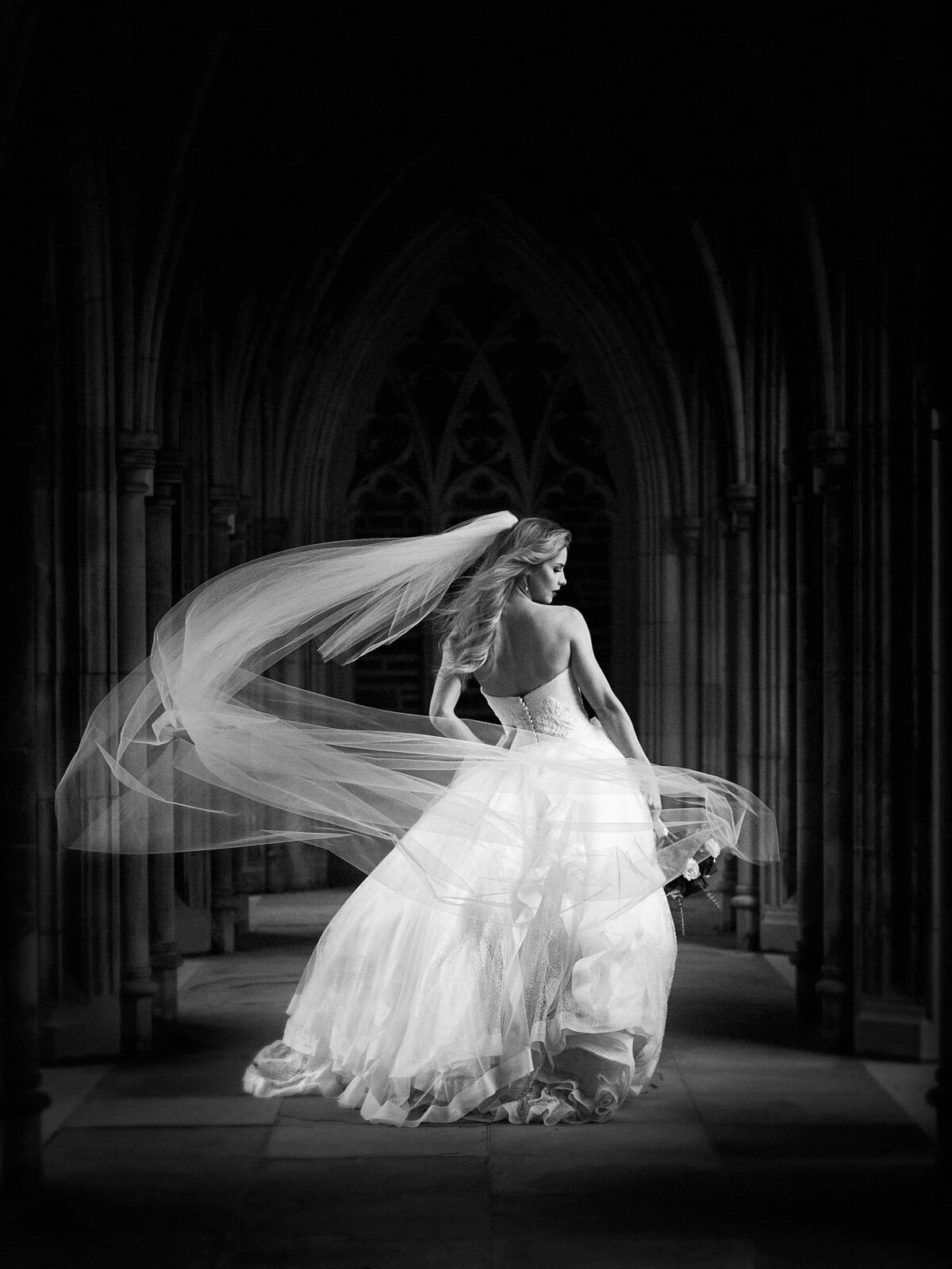 Dramatic black and white image of a bride with her veil flowing around her in the gothic architecture of Duke Chapel's arcades