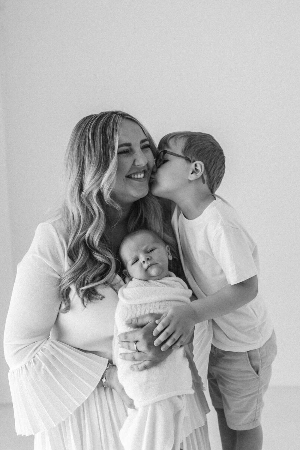 mum, baby and brother in a photo and big brother gives mum a kiss