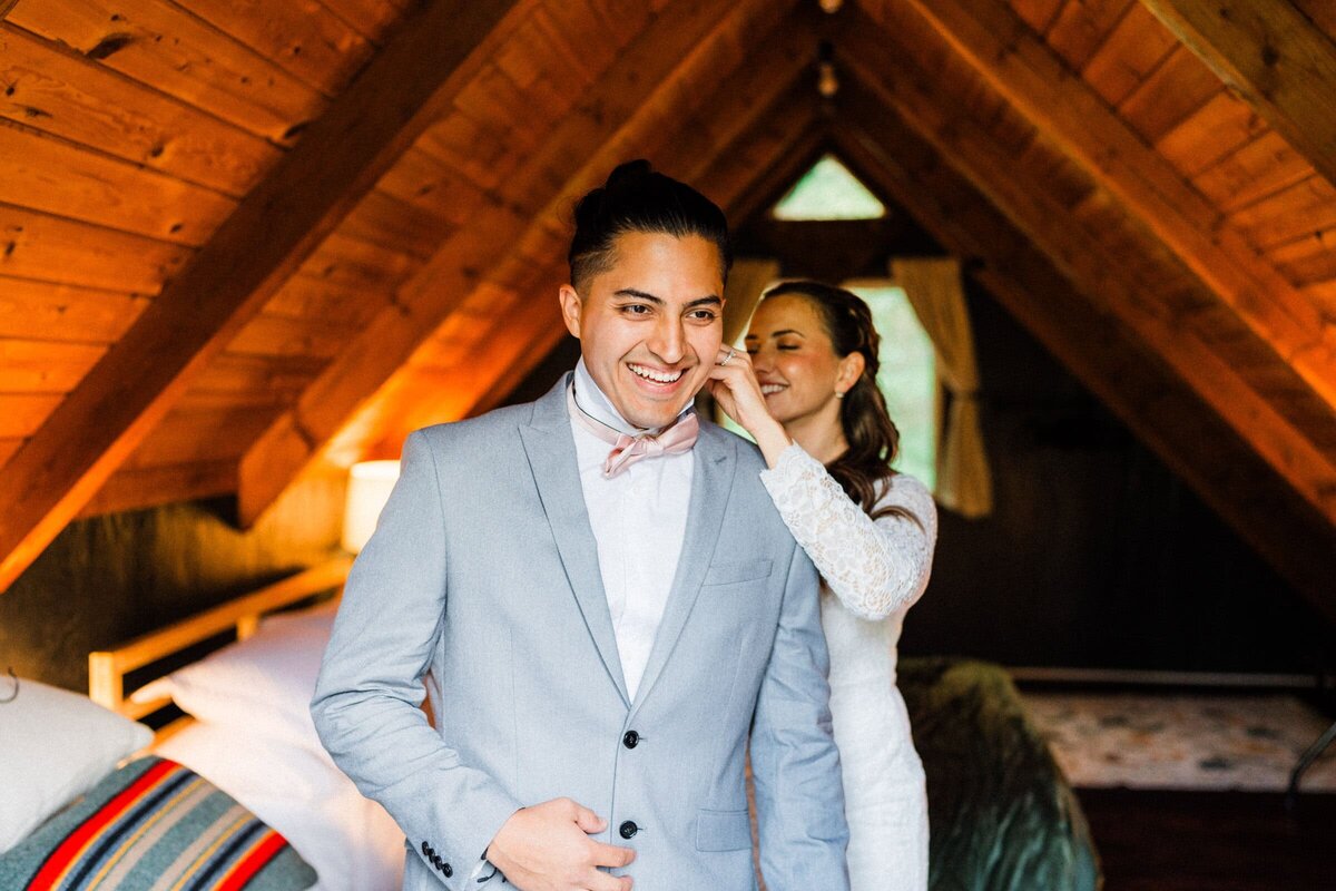 A bride tying bow tie on a groom before elopement in an a frame cabin in Washington.