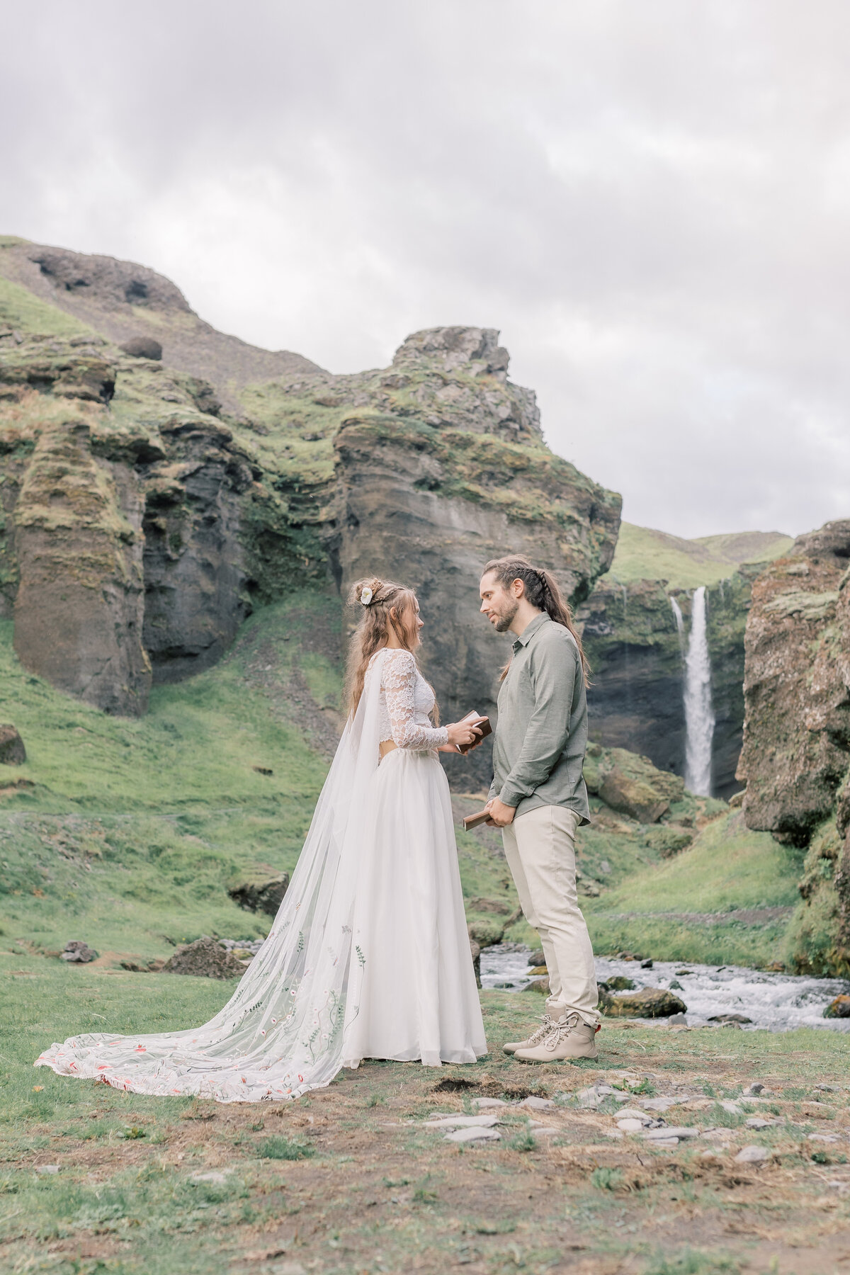 Couple exchanging vows during a private ceremony in front  of a waterfall in a canyon in Southern Iceland.