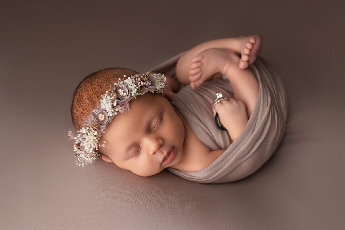 Infant girl wearing a floral headband holding mom and dad's wedding rings.