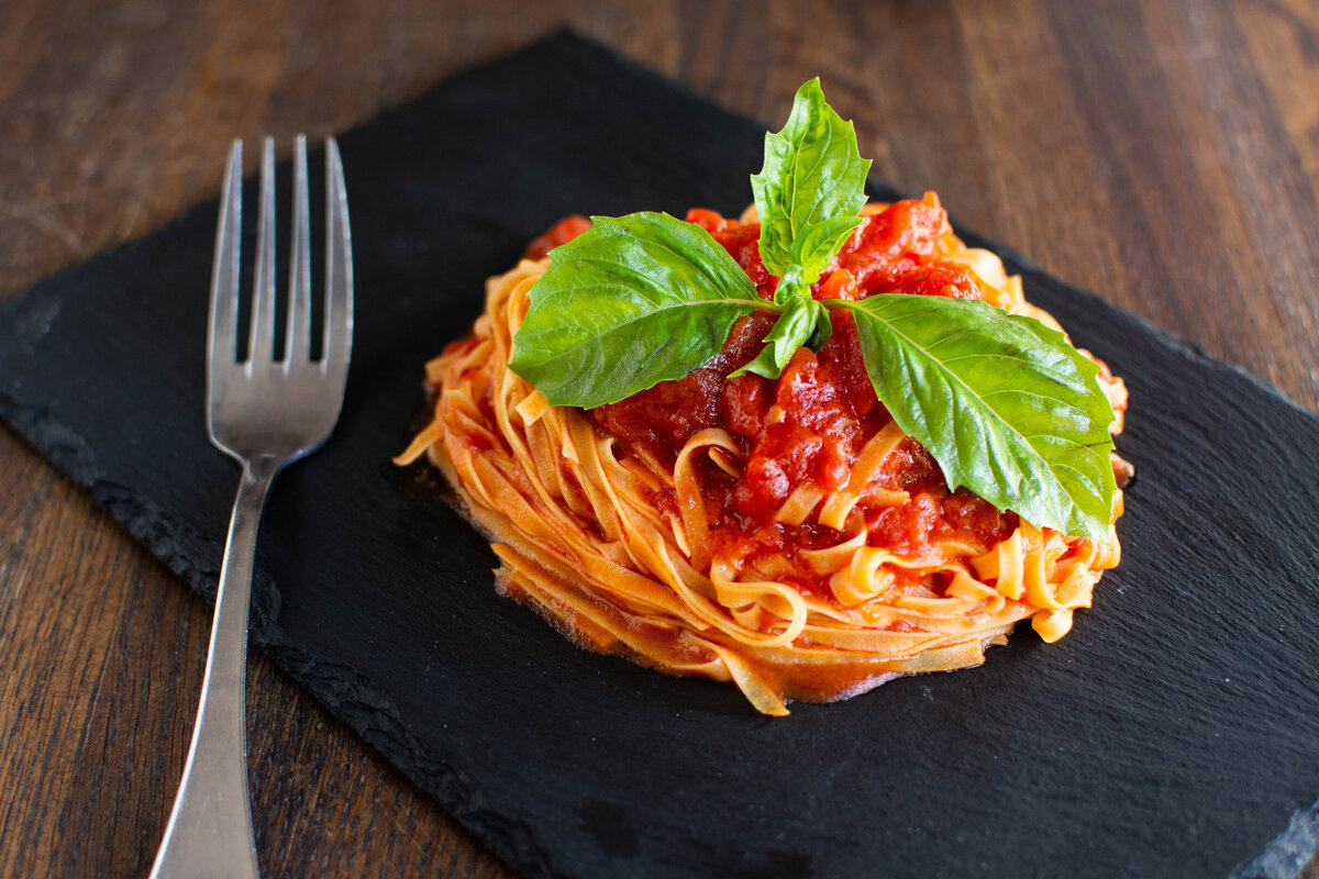 Fresh pasta with tomato sauce and basil garnish on a black plate with fork