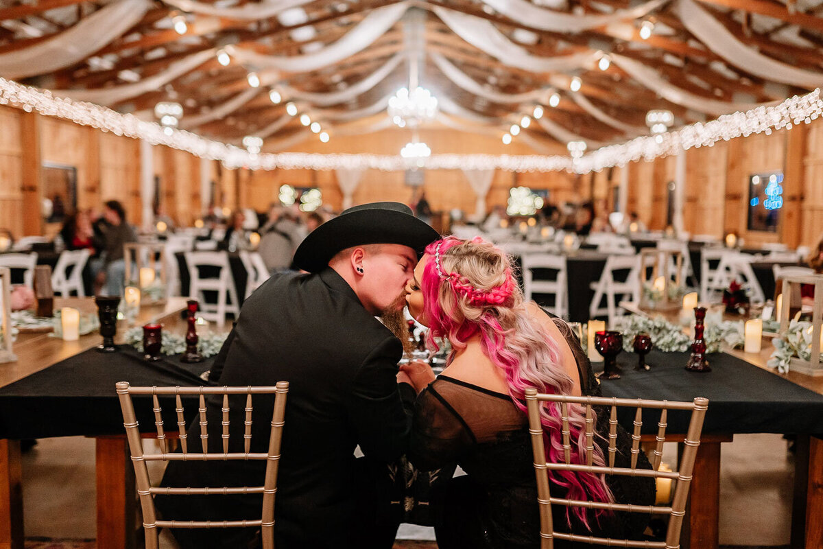Couple with vibrant pink hair kissing at a reception