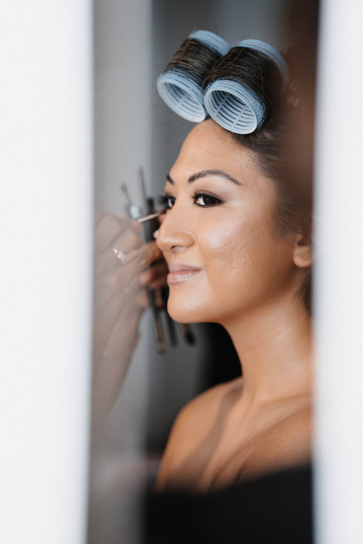 bride with hair in rollers and a hand reaching towards her face with a makeup brush