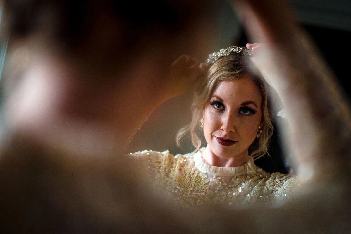 A bride wearing a beautiful headpiece looks into the mirror to look at her reflection