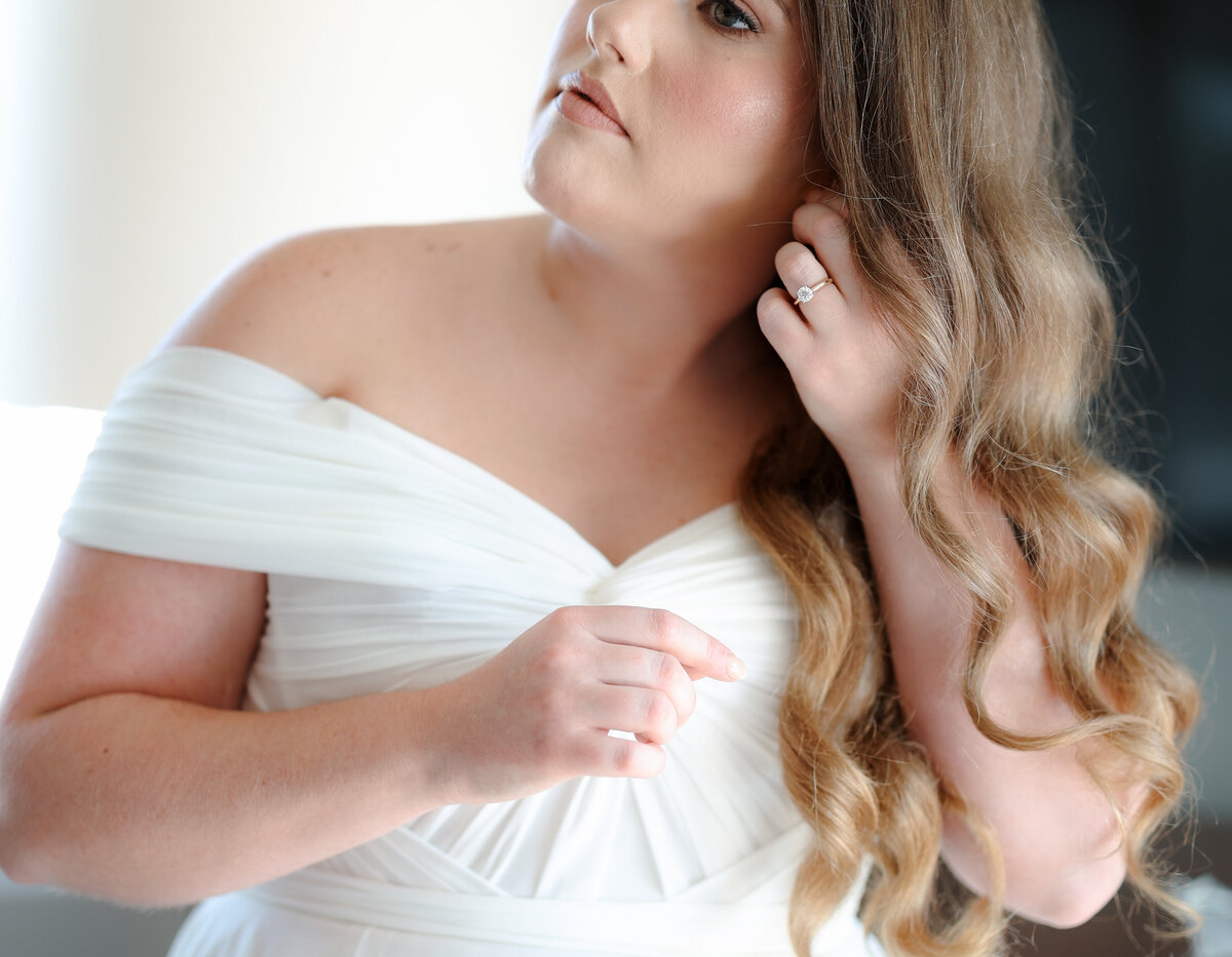 Bride preparing for her wedding day, gently adjusting her veil and dress in a peaceful, light-filled room.