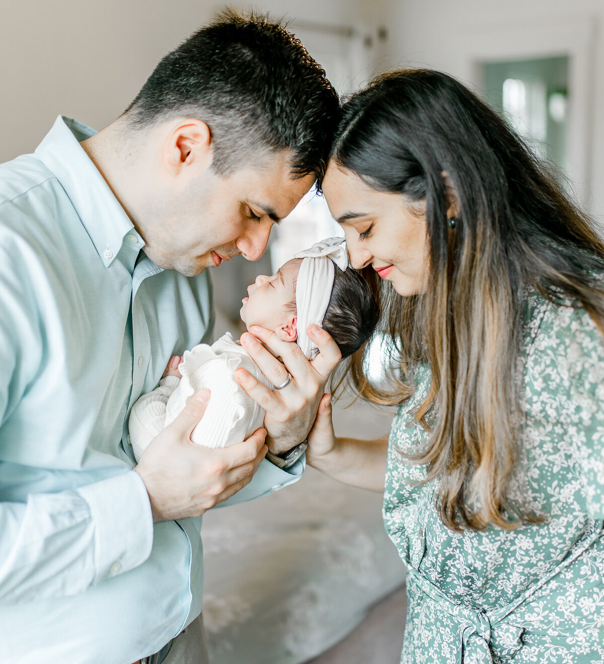 Black and white lifestyle newborn photography featuring a loving couple holding their sleeping baby girl. This intimate family moment highlights the joy of welcoming a newborn at home