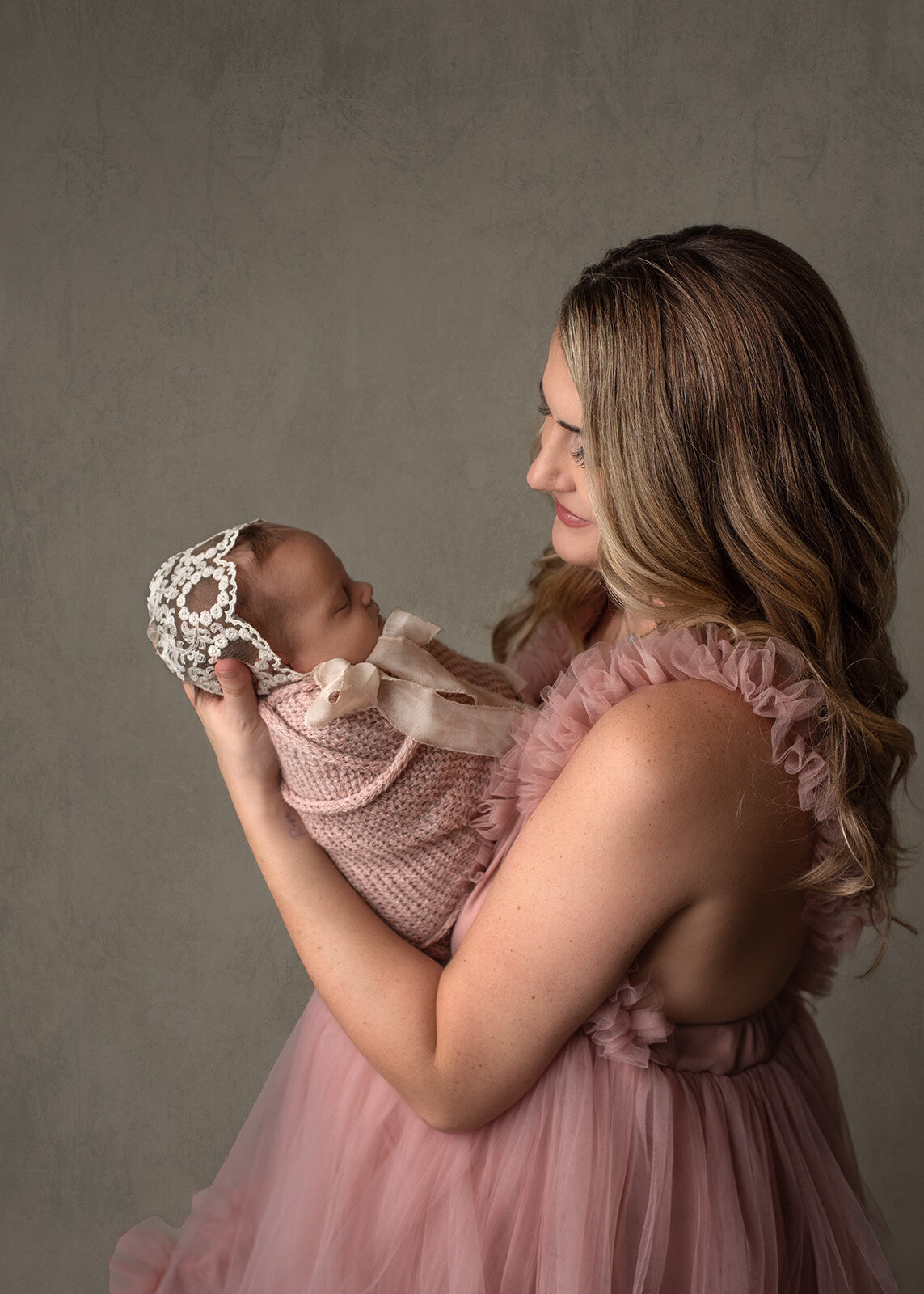 mom in pink tulle dress looking at her newborn in a pink wrap and bonnet by saint louis newborn photographer