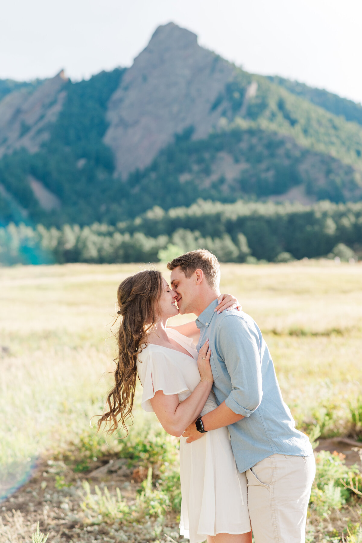 man and woman stand facing each other while the man in the blue top and white shorts leans in for a kiss with the rocky mountains behind them, captured by Denver wedding photographer