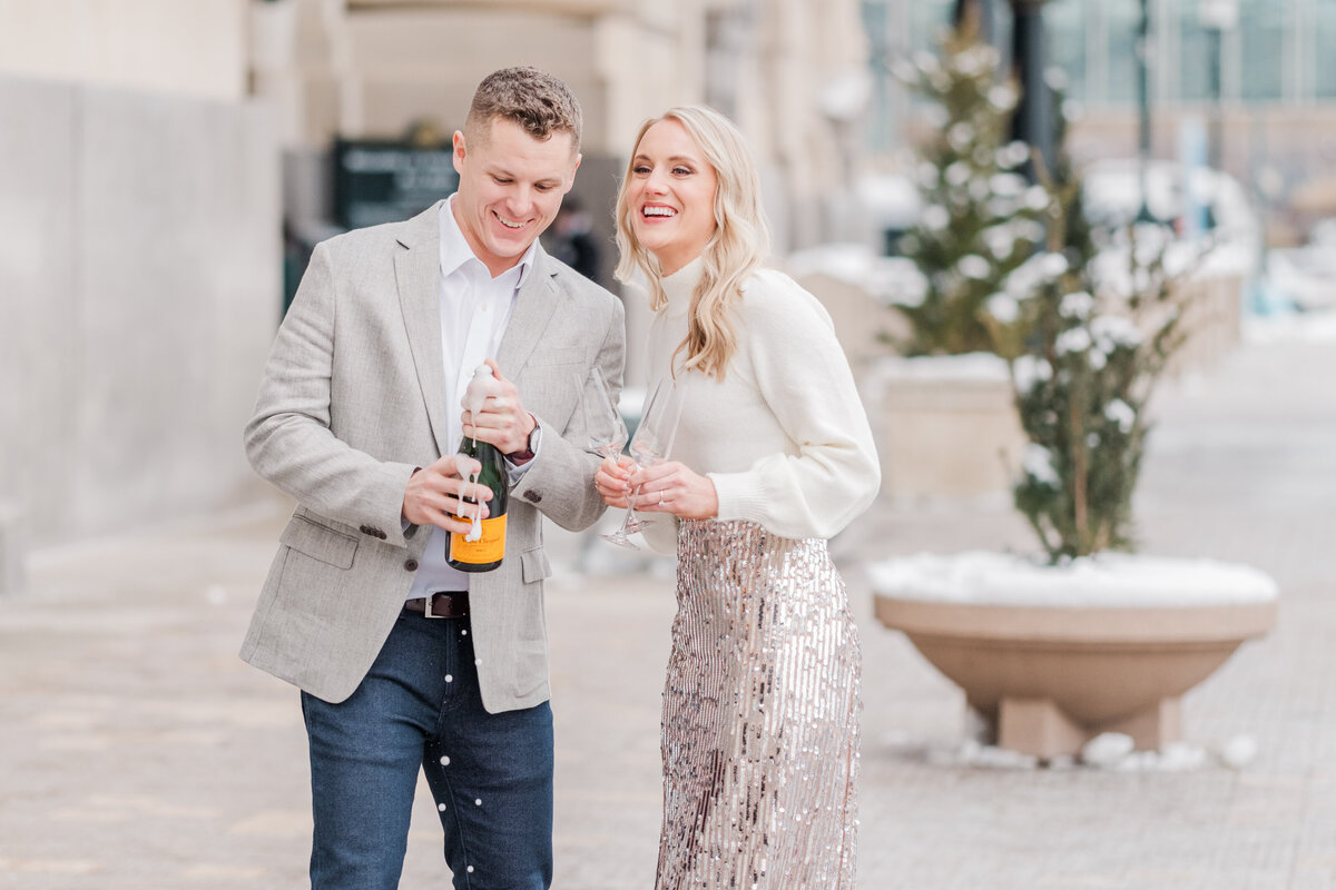 couple wearing sequin skirt popping champagne bottle outside of Union Station during engagement session