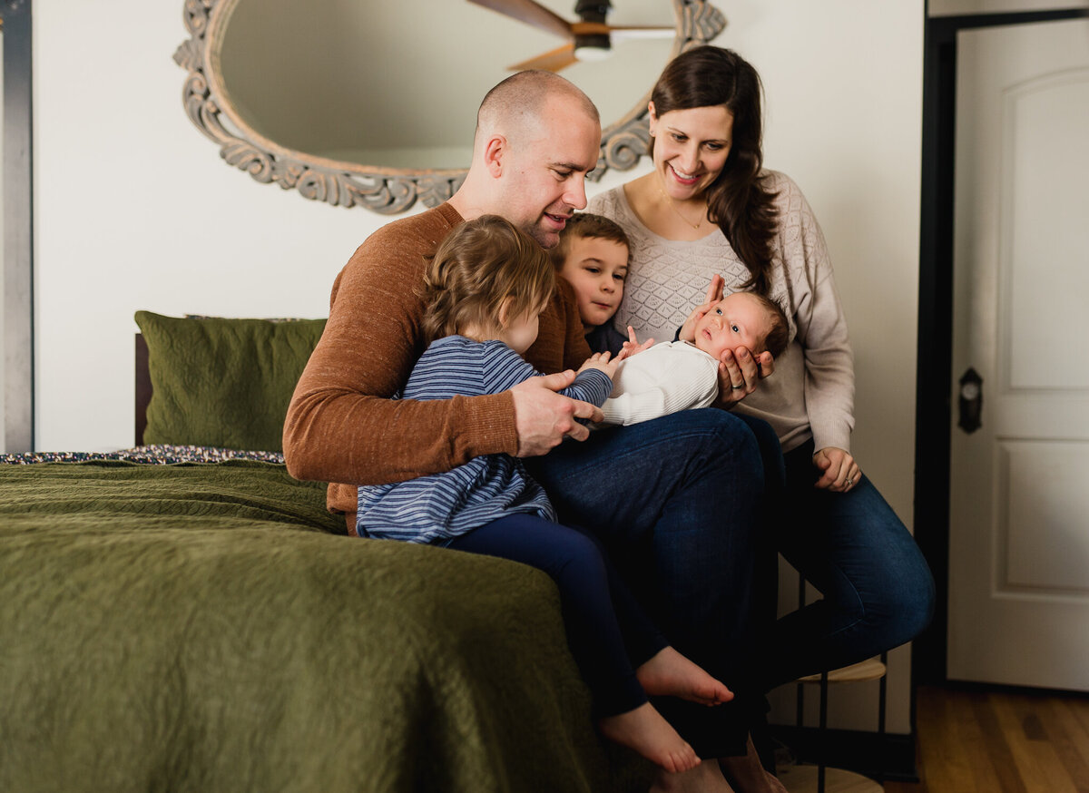 Family photo with mom, dad, children, and newborn baby sitting on bed.