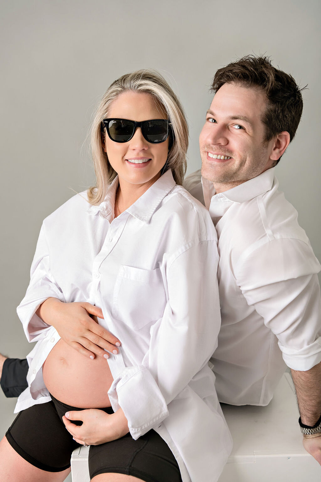 Stylish expecting couple in white button-down shirts for studio maternity portrait