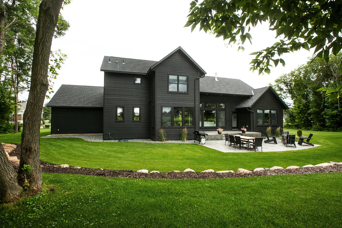 Exterior view of custom home in Otsego, Minnesota with black siding, large patio and windows built by Cornerstone Custom Builds
