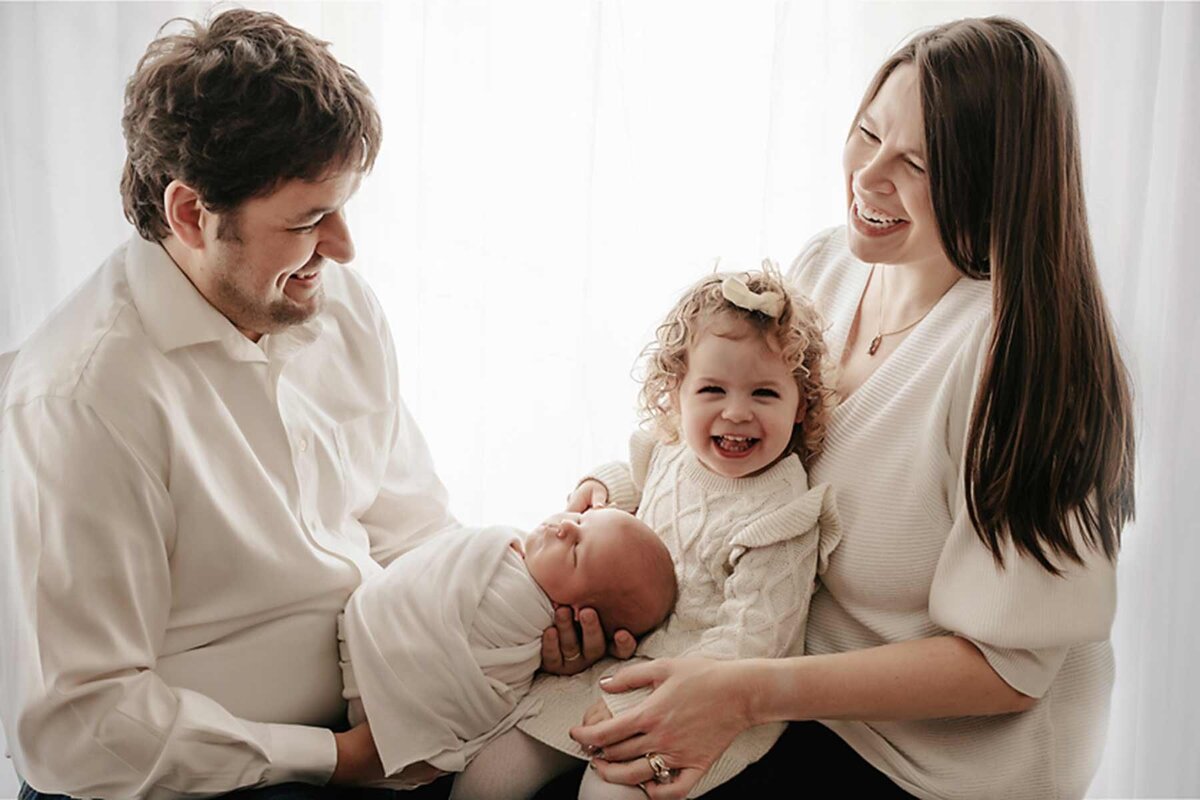 Brightly lit family portrait of a family with their daughter and newborn