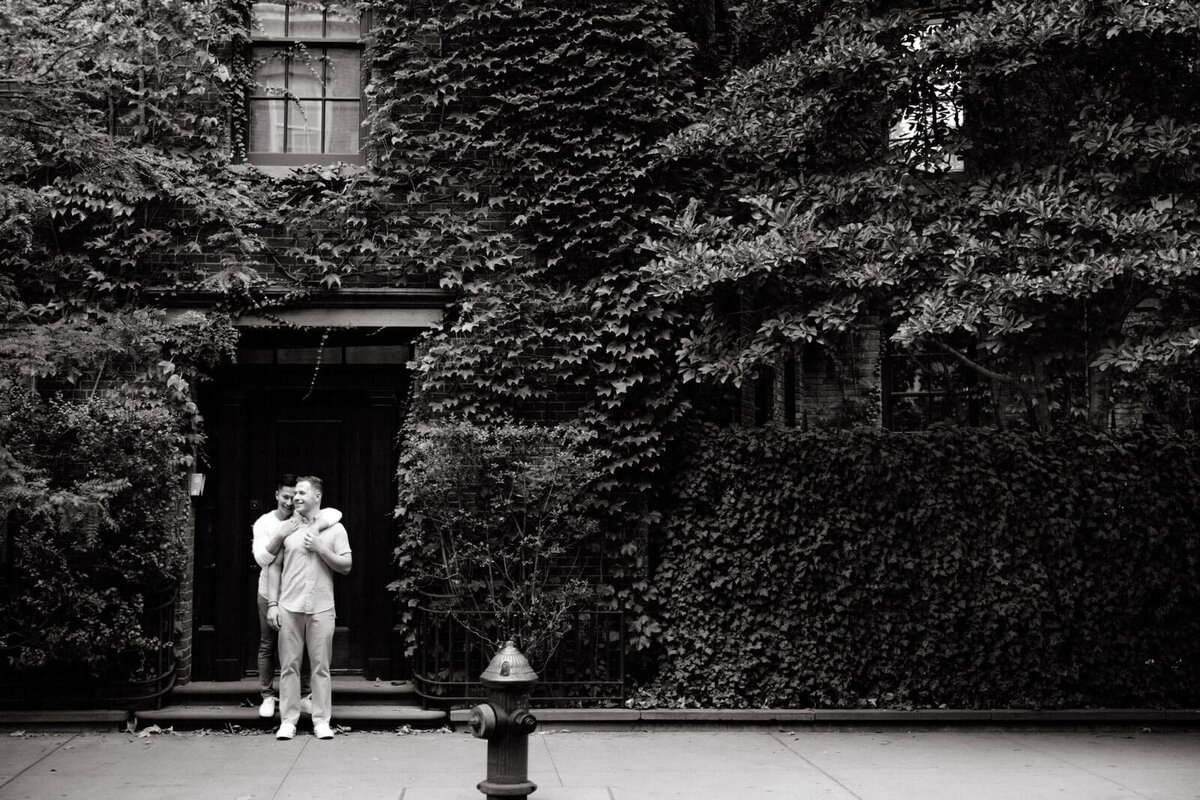 Black and white photo of the engaged couple standing in an ivy-covered building in West Village, NYC. Image by Jenny Fu Studio