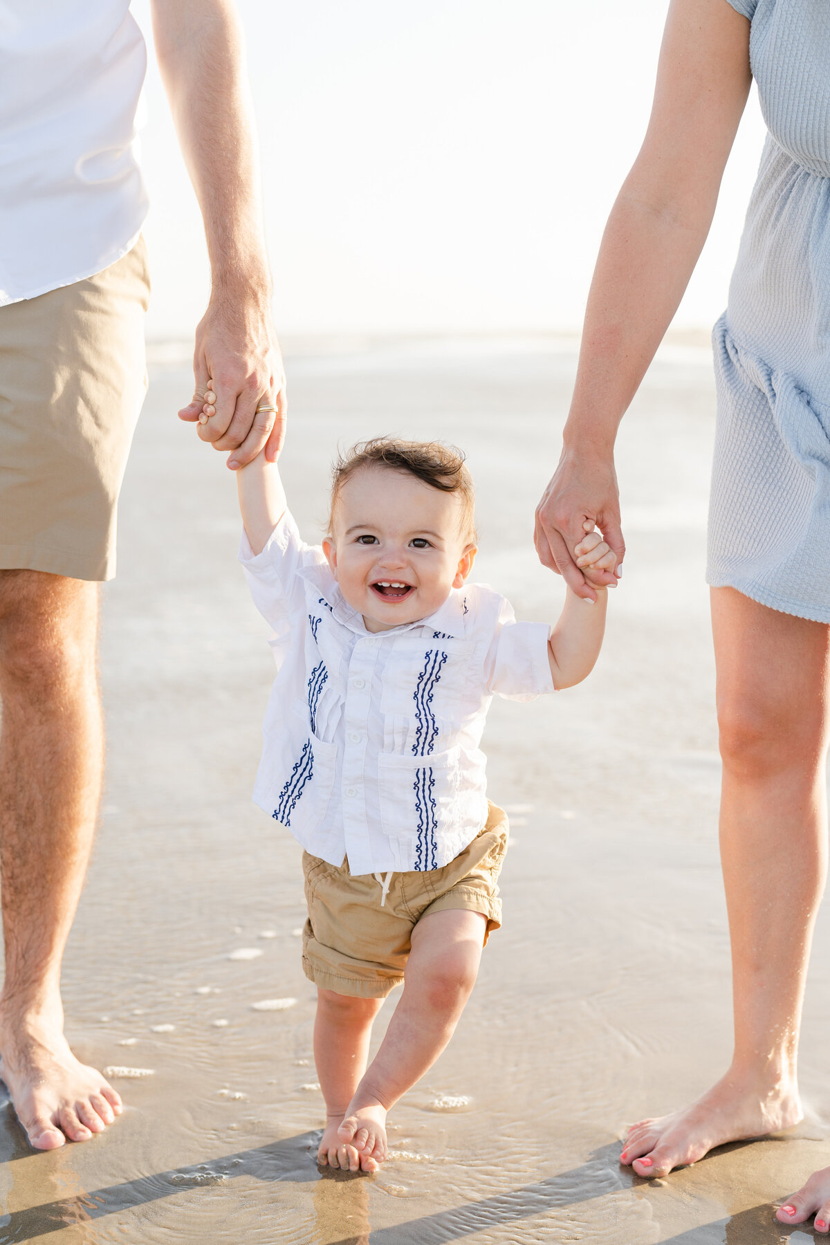 Little boy holding parents hands and smiling while walking on the beach in Galveston Island