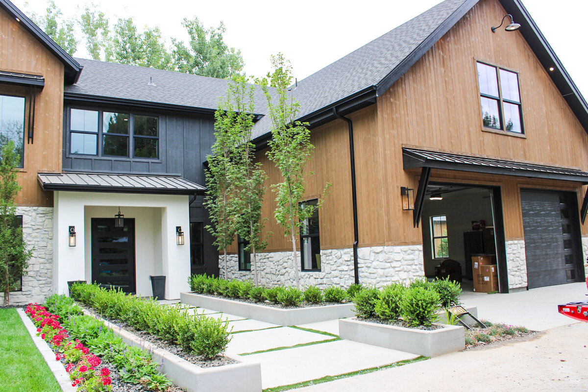new home with black exterior green bushes and red flowers in front yard