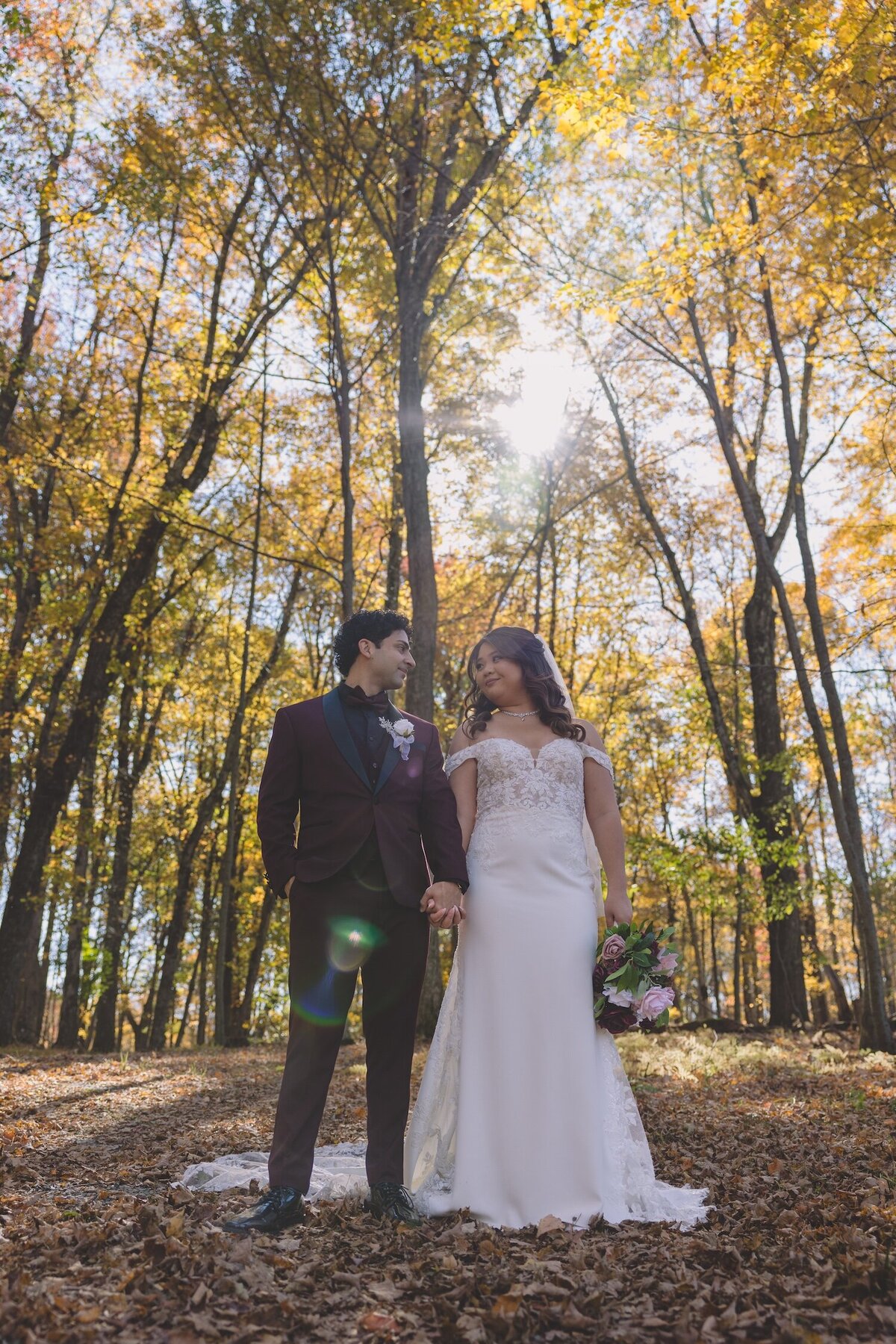 Bride and groom holding hands and smiling under a canopy of fall trees.