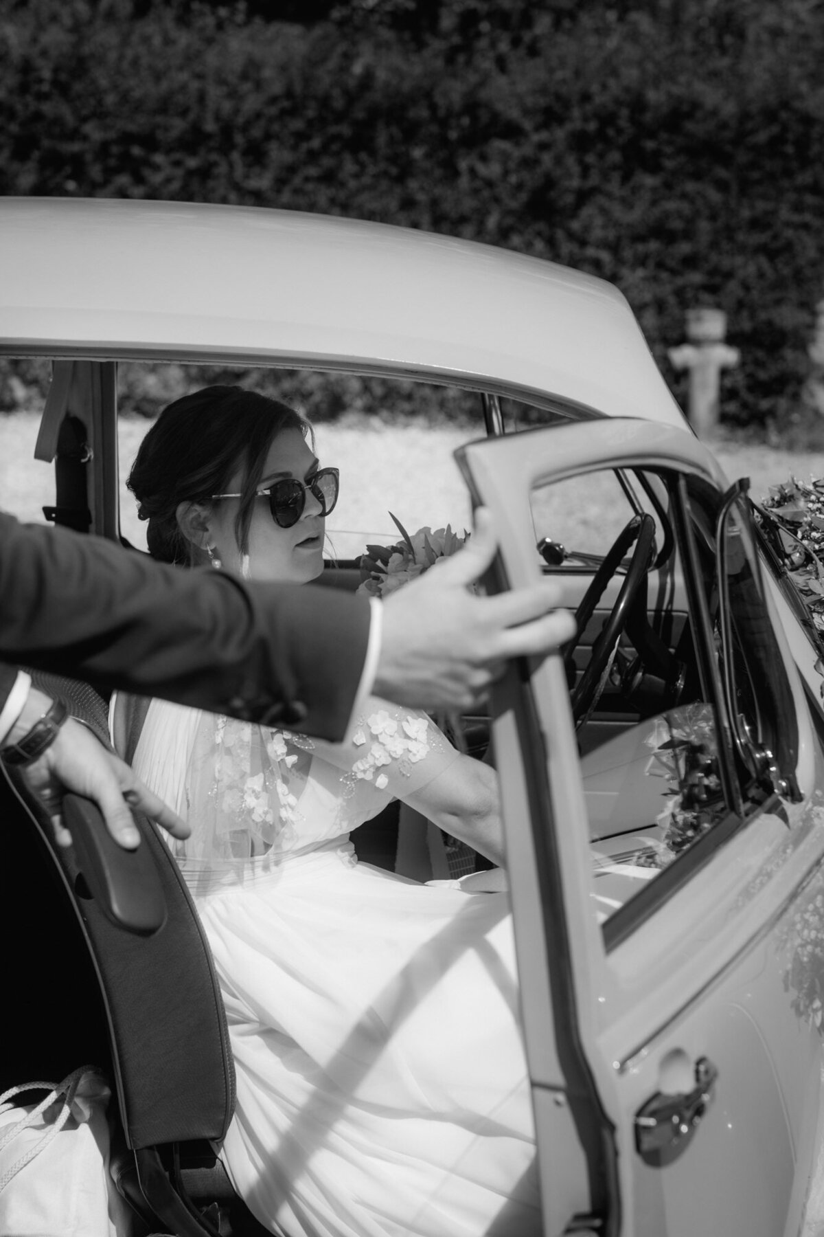 Der Bräutigam hält der Braut die Türe des Hochzeitsautos auf, damit sie aussteigen kann.