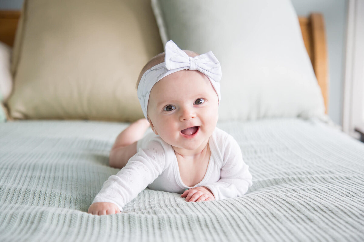 Joyful baby girl laying on her tummy on bed during session with las vegas milestone photographer