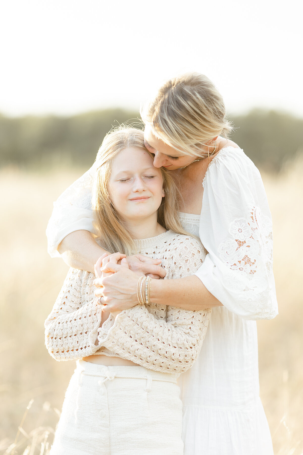 Photo of a mother holding her daughter tightly as her daughter smiles and embraces this moment with her mother as their family photographer captures the moment.