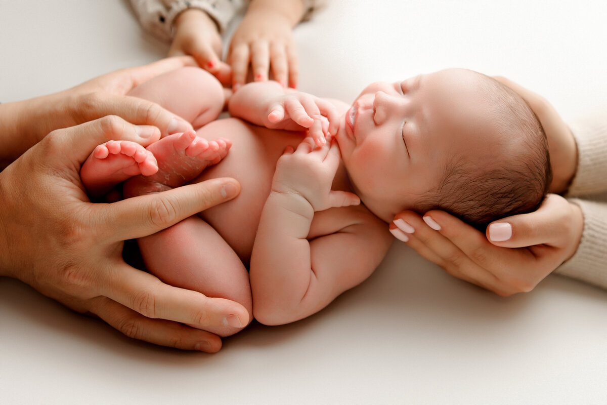 Parents and siblings gently hold hands on newborn baby in Fresno CA photography studio