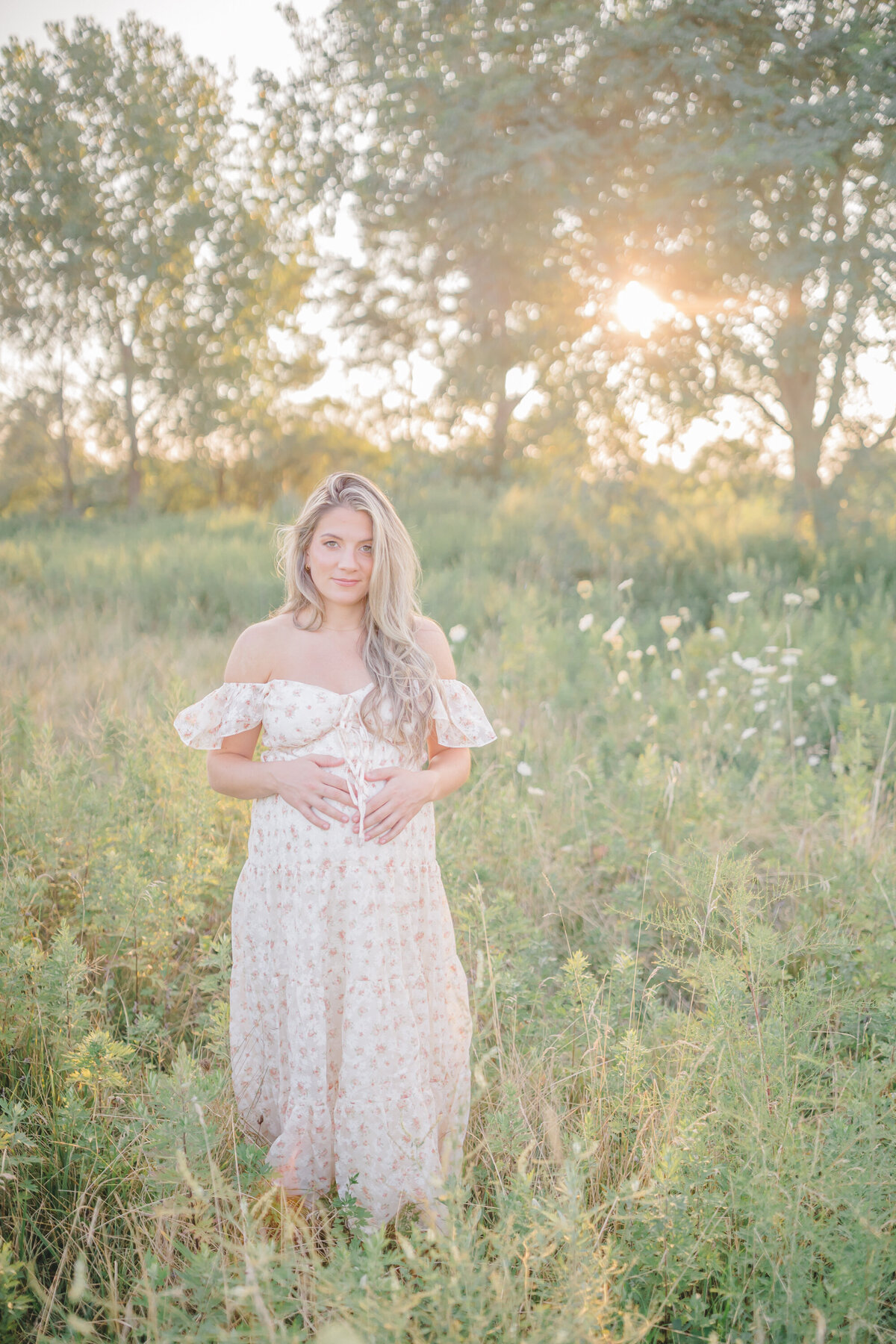Expecting mom in a lavender dress, standing in a golden field at sunset, with soft, warm light illuminating her