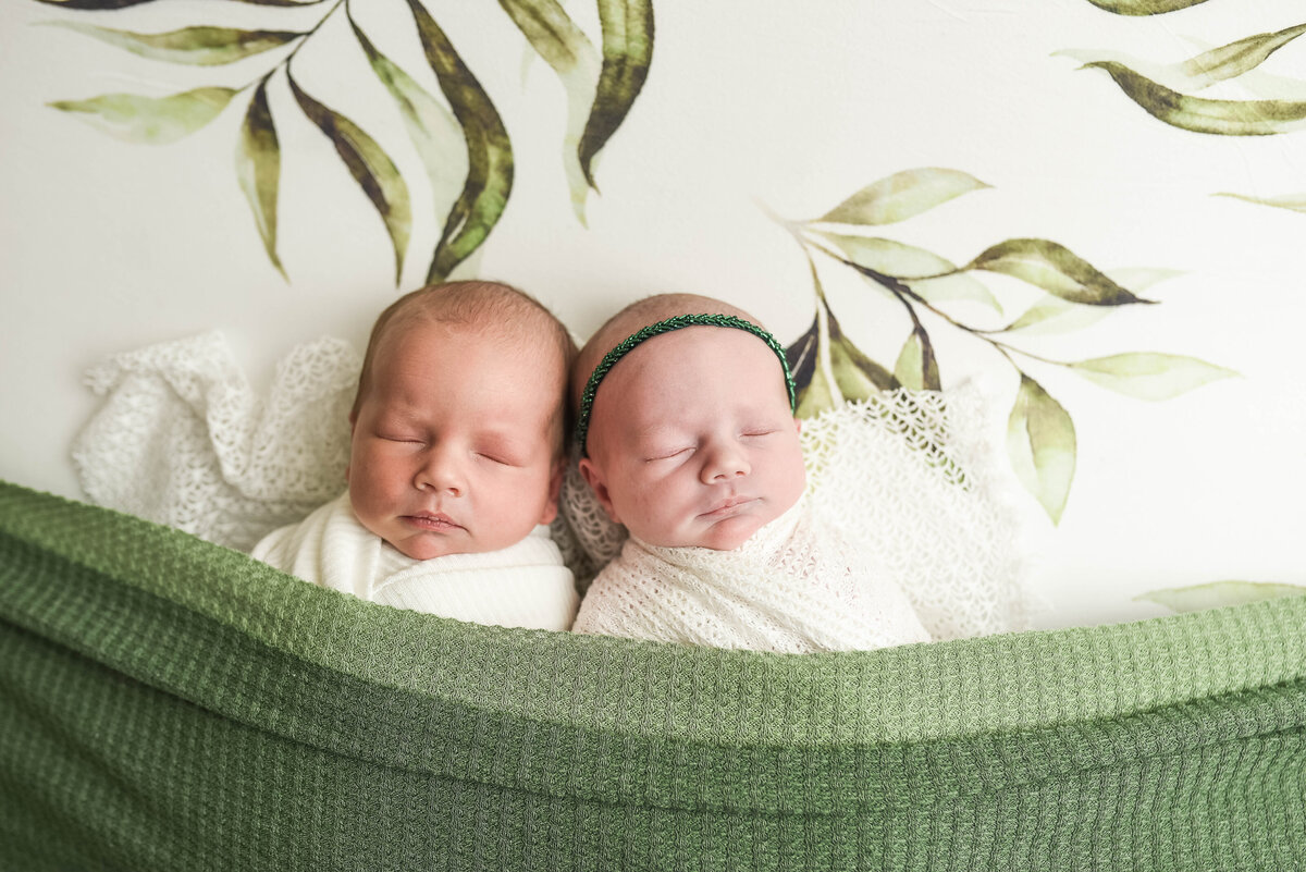 twin newborns covered with green  blanket posing for photo shoot