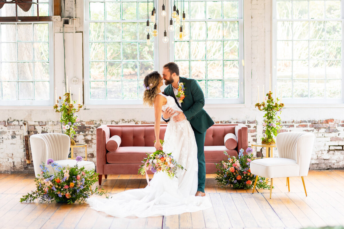 Bride and groom smiling while hugging in front of pink velvet couch