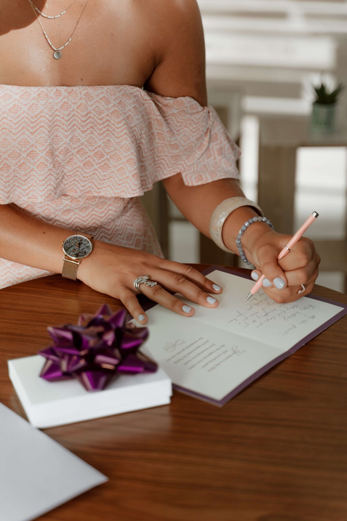 A woman writes out a card next to a present with a bow on a table