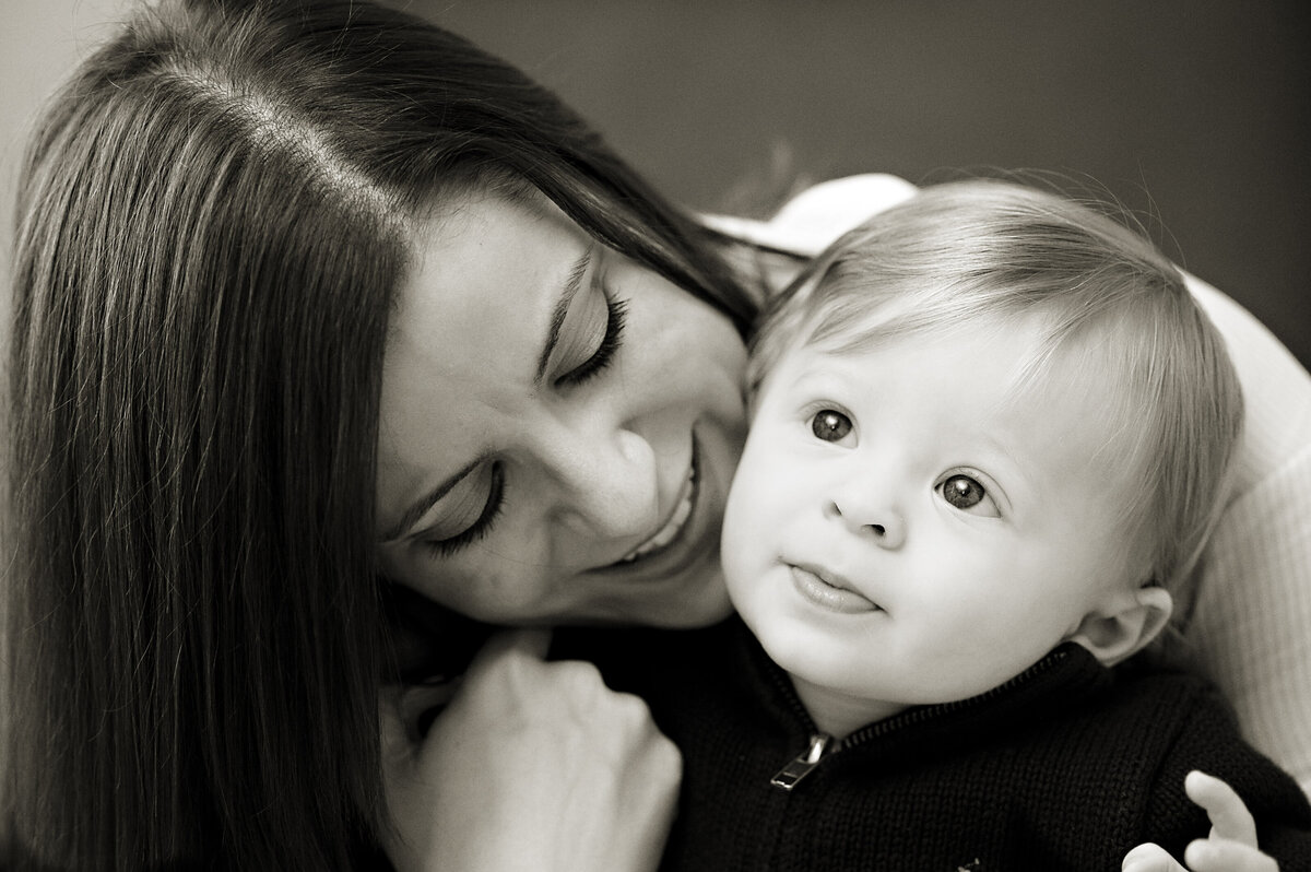 A parent sitting behind their baby as they smile at them