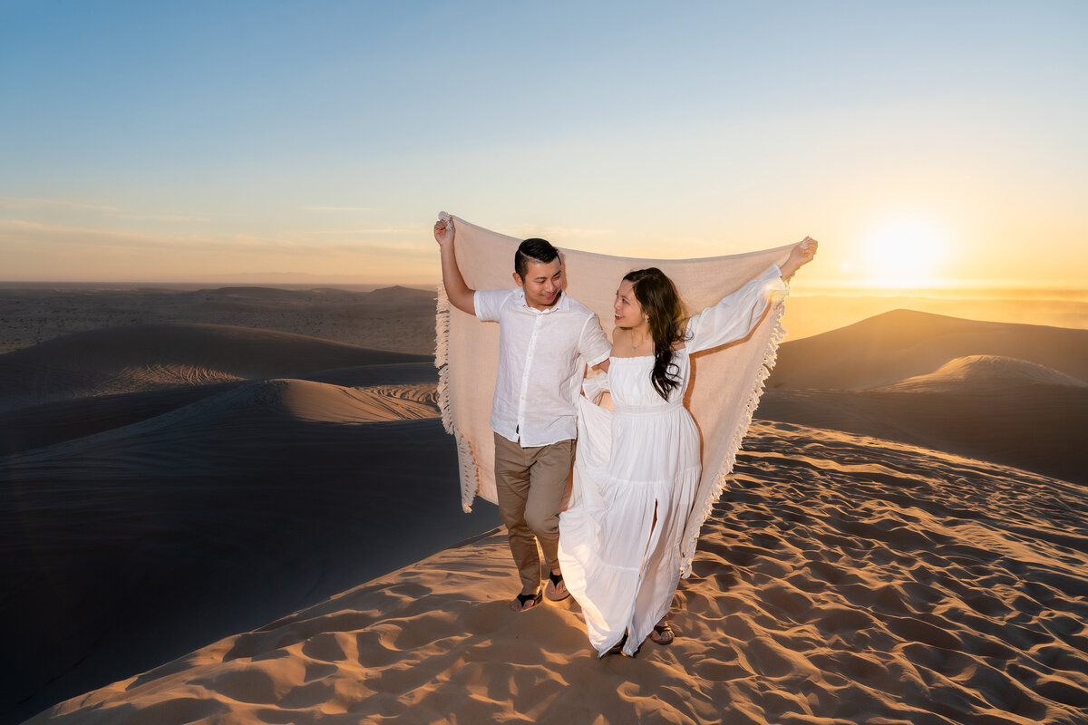 Glamis Sand Dunes elopement bride and groom during sunset walking with blanket.