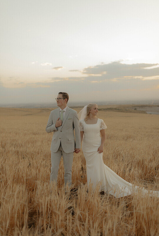 A bride and groom pose for bridal portraits for their wedding. They're standing next to each other holding hands.
